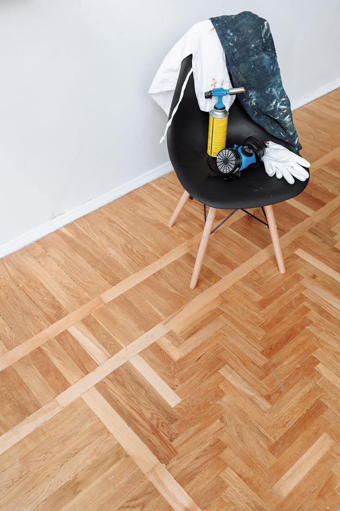 Woodworking tools on chair with parquet floor surface, featuring a blowtorch, gloves, and protective gear.